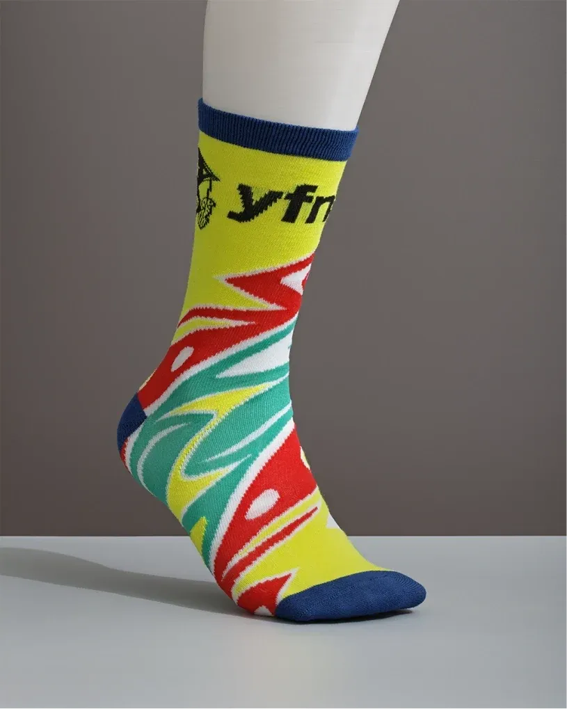 Foot wearing a colourful YFNED crew sock with a yellow, red, teal and blue pattern.
